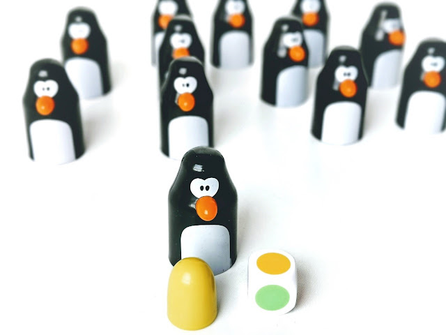 Pingolo gra dla przedszkolaka, na zdjęciu zbliżenie na pingwina z żółtym jajkiem, obok leży kostka z wylosowaną żółtą ścianką a w tle majaczy reszta pingwinów