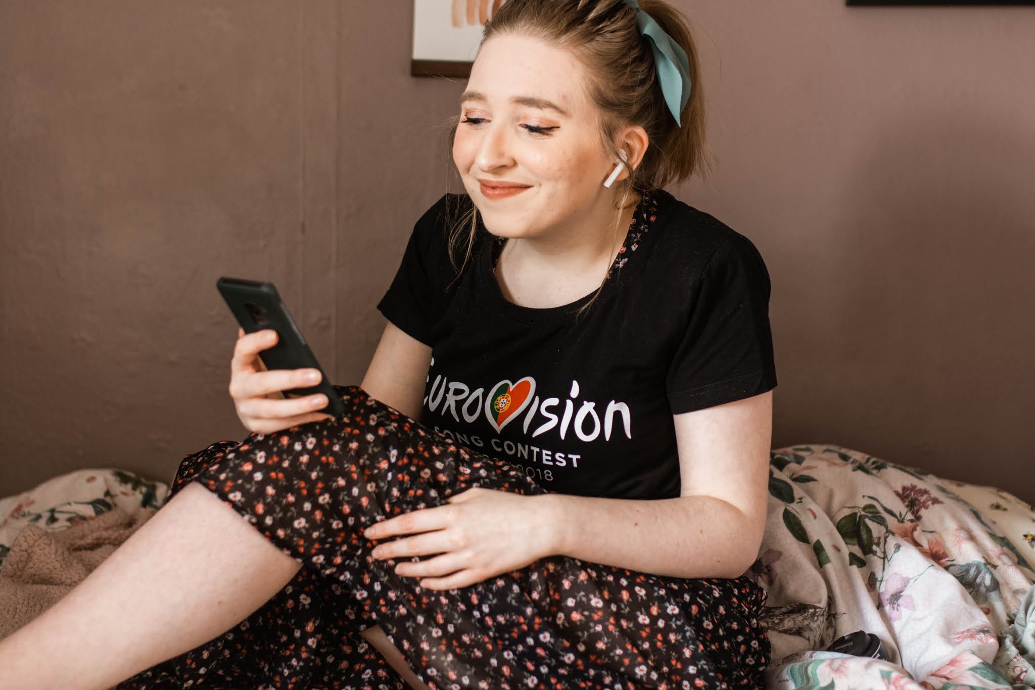 girl smiling with bow in hair listening to music on airpods with eurovision t shirt