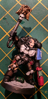 A space marine in black armour holding a ornate weapon aloft. Part of his head has been replaced with metal.