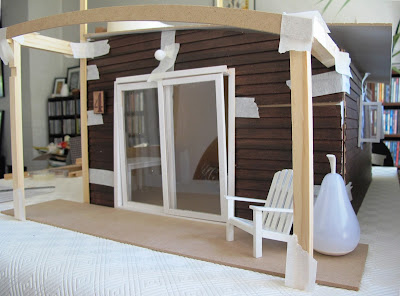 Dry fit of a dolls' house shed kit, with stained weatherboarding taped to the sides and pergola posts and struts taped in place.