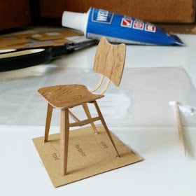Almost completed cardboard model of a 1958 Ercol butterfly chair, set in a jig in front of the tools used to make it.