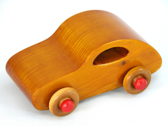 A small handmade wooden toy car classic 1957 bug from the Play Pal series made from pine wood and hand finished with amber shellac. The hubs are painted bright red. Small enought to use as a stocking stuffer or cake topper.