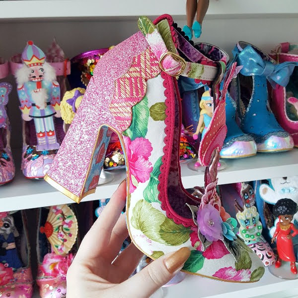 pink floral shoe held in hand with shoe room shelves in background