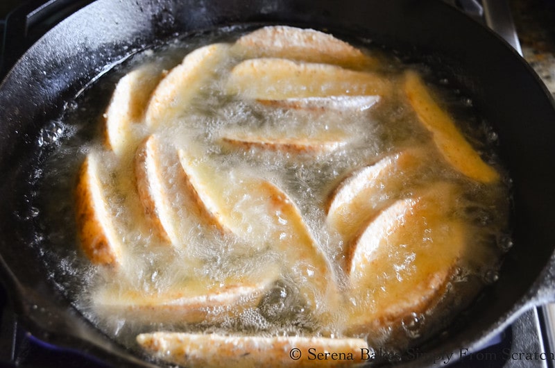 Seasoned Jo Jo Potatoes frying in hot cooking oil in a cast iron pan.