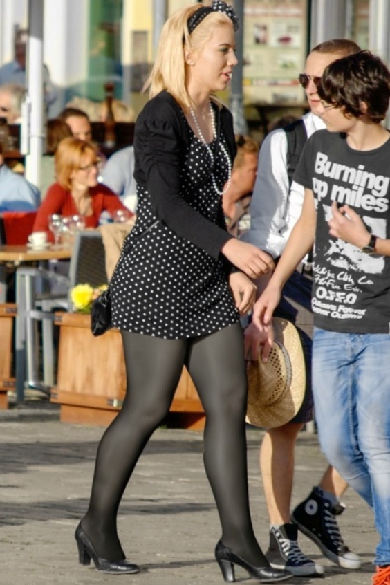 Cute woman walking and wearing a polka dot dress with black tights and heels.