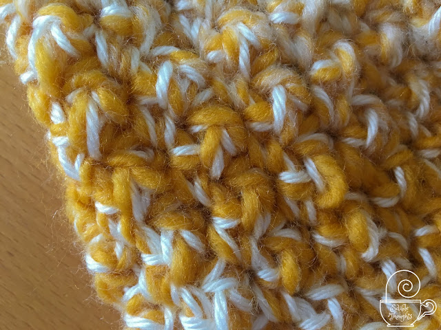 Image is close up of a crocheted cowl made of a bulky yellow and medium weight shimmery cream yarns. 