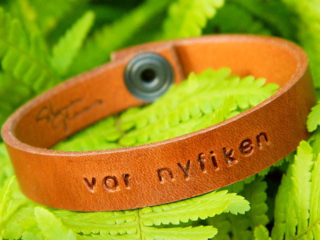 A brown leather bracelet made by Stina Glaas sitting on a green fern