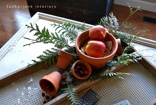 Christmas vignette with apples, evergreen branches inside plant pots on an antique soil sifter. Perfect for tv remotes!