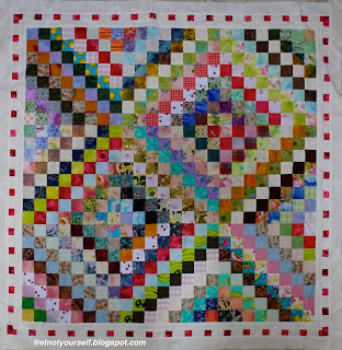 A small quilt of nine Scrappy Trip blocks is bordered in pink and white.