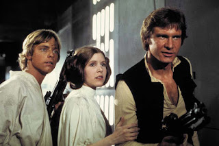 Luke, Leia e Han Solo lado a lado, todos observando algo extracampo. Luke segura uma arma, Han aponta a arma dele para quem eles observam e Leia segura o braço de Han.