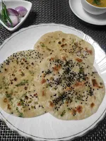 Serving 3 pieces of kulcha in a plate, dal and onion slices in background