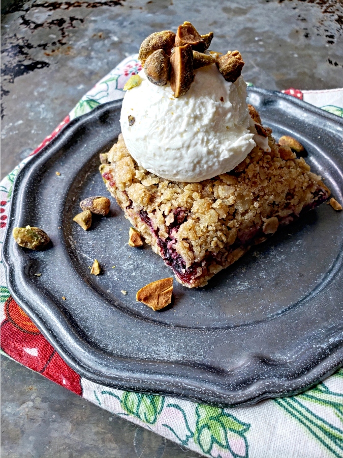Cherry and oats bar dessert on a plate topped with frozen yogurt and pistachios
