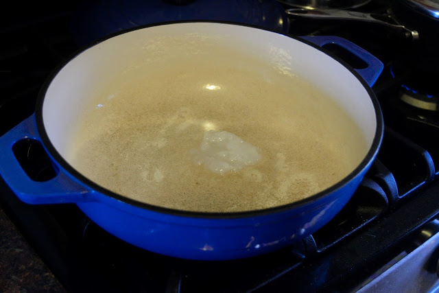 A dutch oven, sitting on the stove, with coconut oil in it. 