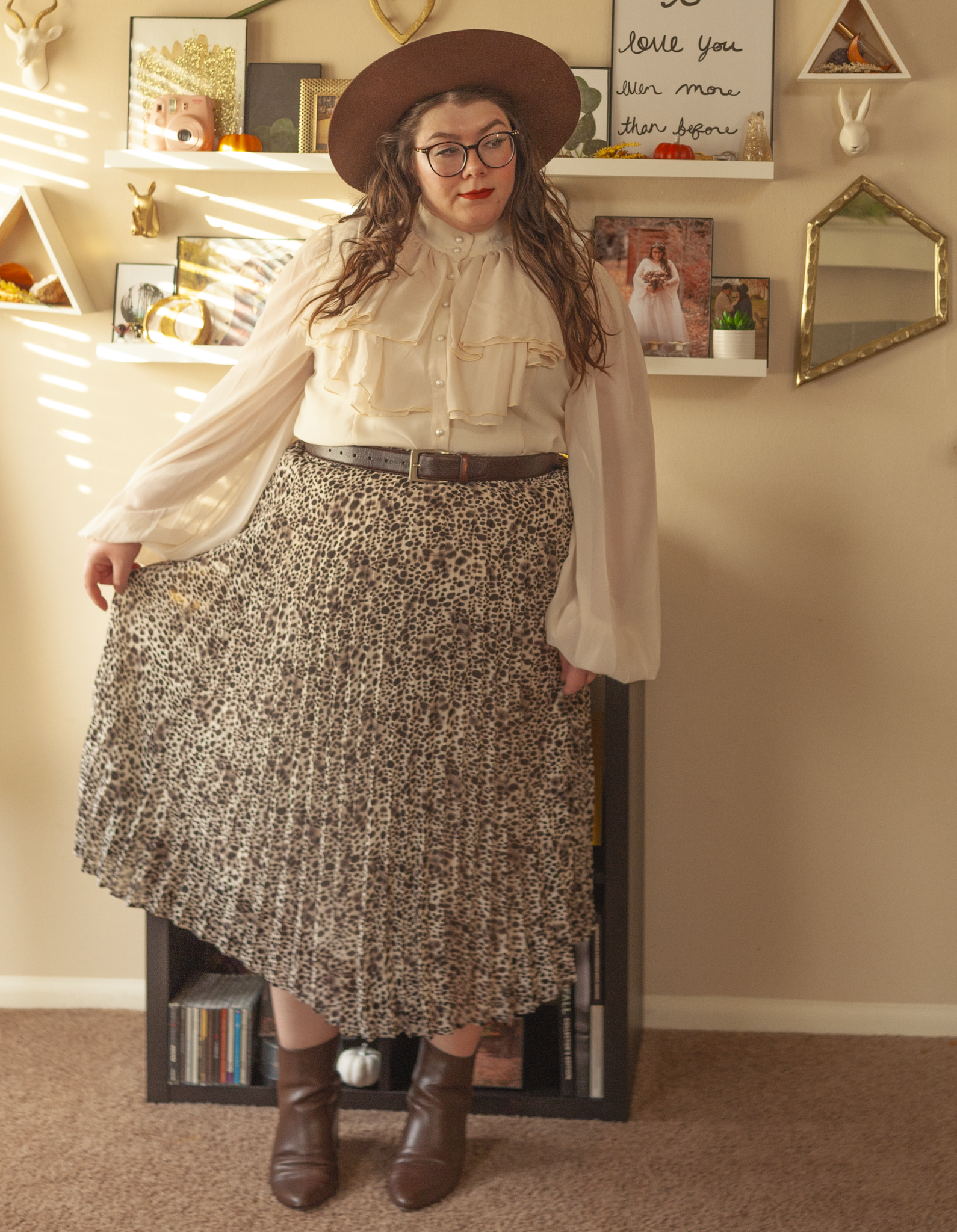 An outfit consisting of a cream high neck Regency inspired long sheer bishop sleeves with a ruffle bodice, tucked into a cream and black leopard print pleated midi skirt and brown midi boots.