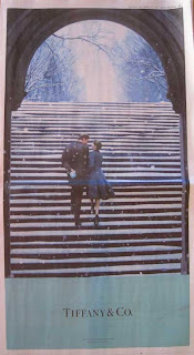Full page newspaper ad for Tiffany & Co. with light turquoise, black and white color scheme, showing a young man and woman walking up a snowy staircase toward an arch with snow-covered trees