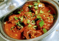 Serving chicken lollipop gravy in a bowl topped with spring onions