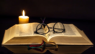 Biblia abierta, candela encendida y lentes