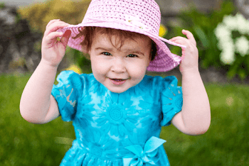 A smiling toddler with a straw hat on the head