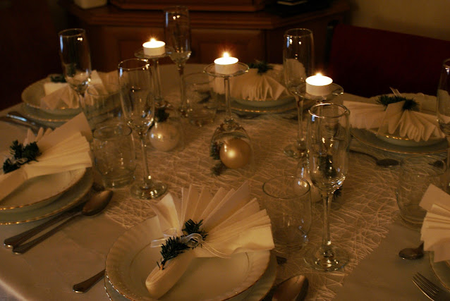 stół wigilijny z białą zastawą, świecami i ozdobionymi stroiszem serwetkami
