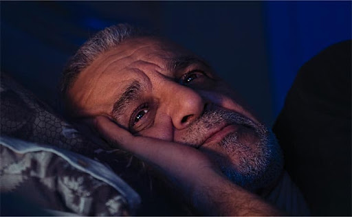 homem de meia-idade acordado na cama em um quarto escuro
