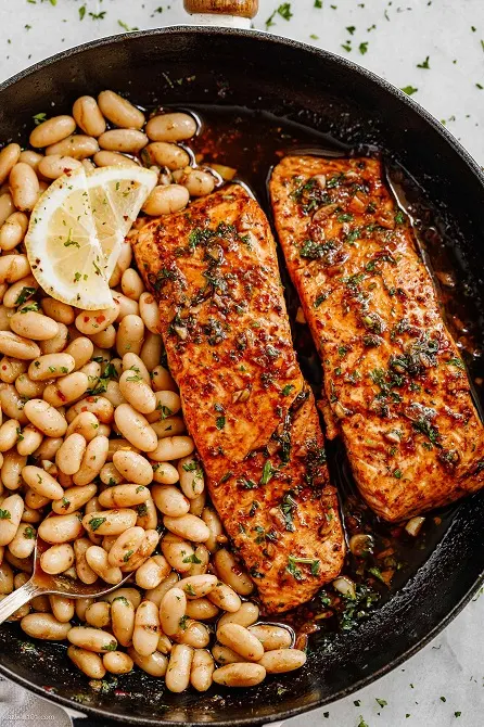 Garlic Butter Salmon and Lemon White Beans Lemon Garlic Butter Salmon with White Beans – A complete meal in one pan using minimal ingredients you already have in your kitchen! This garlic butter salmon is full of flavor and so easy to make! Salmon is marinated and pan-seared to flaky perfection, then creamy cannellini beans are tossed in the lemon garlic butter sauce and develop a rich, rustic flavor. This salmon and white bean recipe is an easy and delicious weeknight meal everyone will love. Enjoy! INGREDIENTS LIST FOR THE GARLIC BUTTER SALMON AND WHITE BEANS : 1 lb (450g) salmon filets, cut into 2 chunks 2 15oz cans cannellini white beans 1 tablespoon olive oil 1 tablespoon low-sodium soy sauce 2 teaspoons minced garlic 1 tablespoon hot sauce, optional (we used Sriracha) Juice of 1/2 lemon, divided 1/2 cup (125ml) low-sodium vegetable broth (or white wine) 1/2 stick butter 1 tablespoon minced parsley (or cilantro) Crushed red chili pepper flakes, optional Slices of lemon, for garnish DIRECTIONS : 1. To make the garlic butter salmon and cannellini beans: In a mason jar or a bowl, combine olive oil, minced garlic, soy sauce, hot sauce, lemon juice, salt, and pepper. Arrange salmon fillets in a shallow plate and pour the marinade over. Let sit while you prepare the white beans. 2. Wash and drain the beans in a colander. 3. Heat olive oil in a large cast-iron skillet over medium-low heat. Drain salmon fillets from the marinade and add to the skillet. Lower the heat and gently cook on both sides until golden brown. Salmon must cook on low to avoid burning the skin and marinade. Remove the salmon fillets from the skillet and set them aside to a plate. 4. Deglaze the skillet with vegetable broth. Bring to a simmer. Add butter, lemon juice, and the remaining salmon marinade. Give a quick stir to combine. Bring to a simmer. 5. Add the drained white beans and toss for 2 minutes to cook up in the sauce. Push beans to the side and add salmon back to the pan and reheat for another minute. Garnish with more parsley, crushed chili pepper, and lemon slices, and serve the garlic butter salmon and white beans immediately. Enjoy!