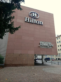 Seitenfassade des Hiltons. Ein großer Block Wand mit Hilton und Fitness First Logo.