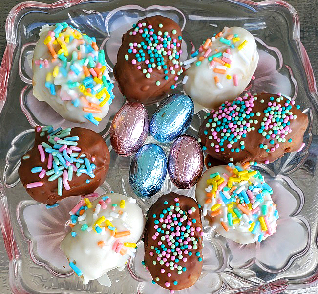 This is a glass Lenox tray on a pedestal of sugar cookies made into truffle candy cookie dough with pastel sprinkles on a melted dipped dry chocolate. The truffles are egg shapes for Easter