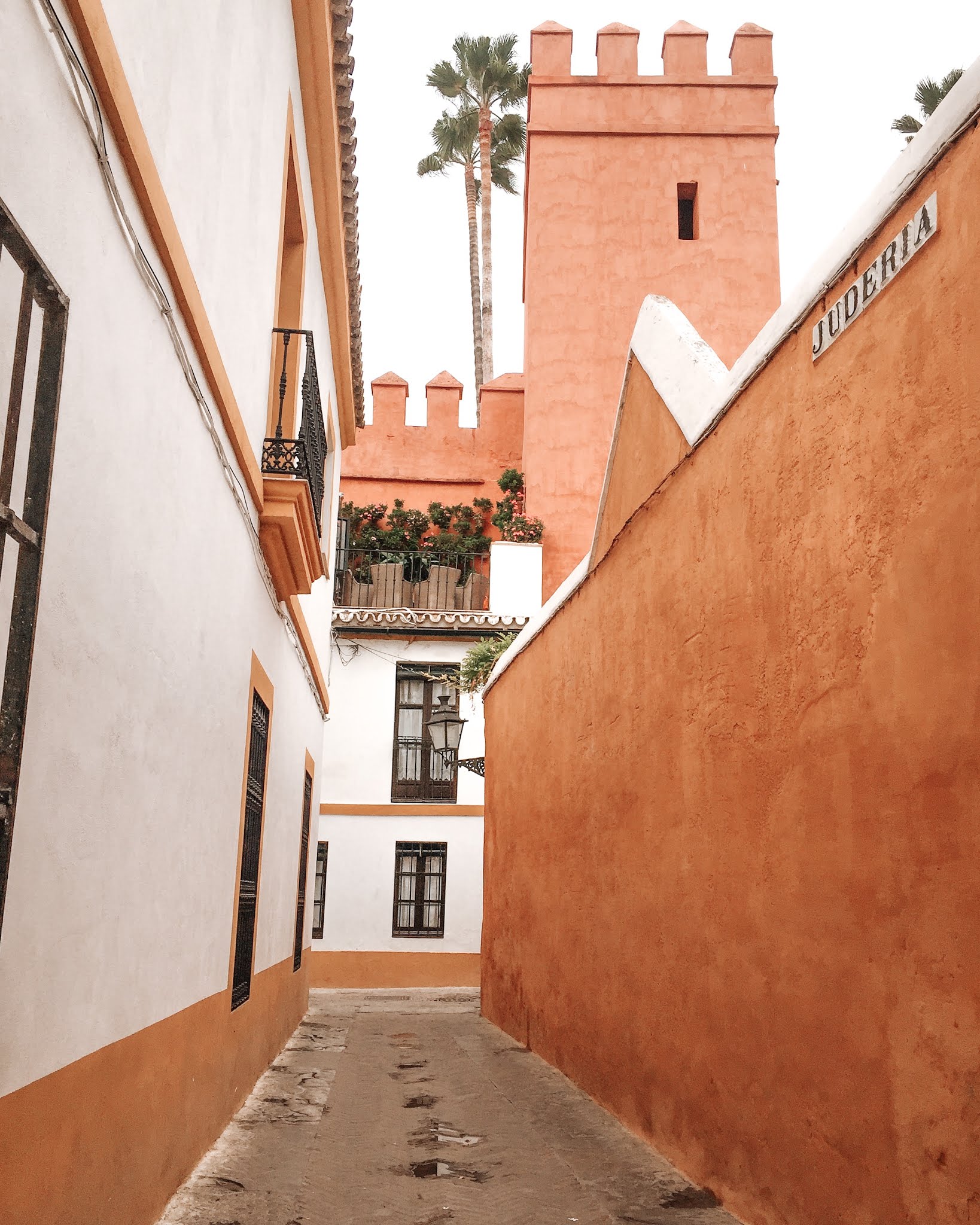 L'une des ruelle du quartier de santa cruz à séville avec une tour orange en fond et des murs oranges et blancs sur les côtés