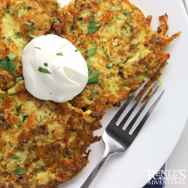 zucchini carrot fritters over head with sour cream and a fork on a plate ready to eat