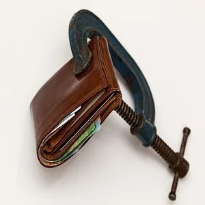 Imagem de uma carteira masculina na cor marrom fechada, com dinheiro dentro, disposta sobre um fundo branco e apertada por um pegador de ferro ilustrando texto sobre tributação no direito de superfície.