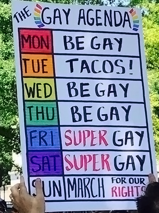 A sign reads, "The Gay Agenda - Monday, Be Gay; Tuesday, Tacos!; Wednesday, Be Gay; Thursday, Be Gay; Friday, Super Gay; Saturday, Super Gay; Sunday, March for our Rights"