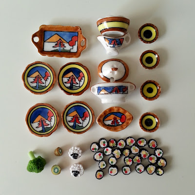 Selection of dolls' house crockery and food arranged on a tabletop.