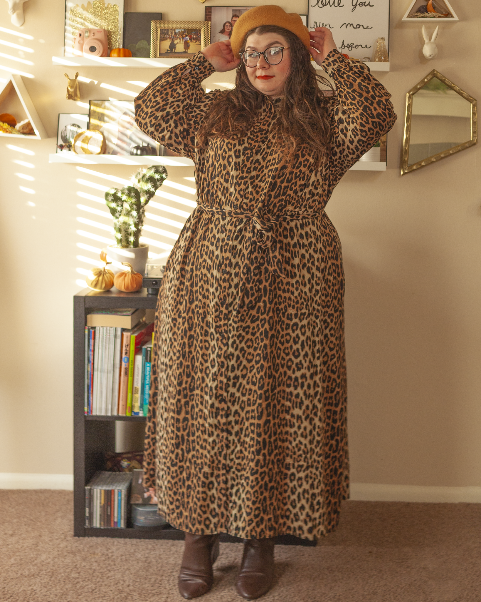 An outfit consisting of a camel brown beret, long sleeve leopard print button down maxi dress, tied around the waist with a connected leopard print tie, and brown midi boots.