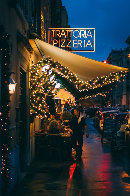 Open-air pizzeria with a lit up neon LED sign spelling out, "Trattoria Pizzeria."