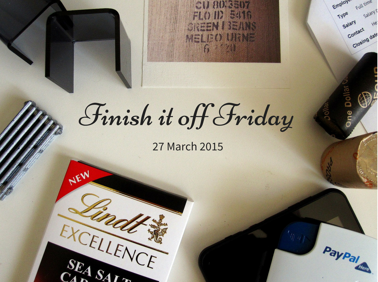 A selection of items laid out on a desk, including a dolls' house miniature radiator and two small tables, fabric printed with a coffee bag, a job advertisement, two rolls of coins, a Paypal Here device and tablet and a block of Lindt sea salt caramel chocolate.