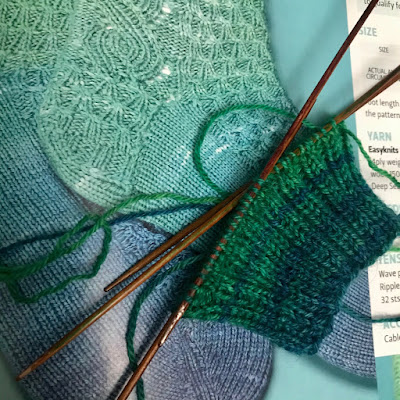 The cuff of a sock knitted on four double-ended needles, lying on a photograph of a sock.