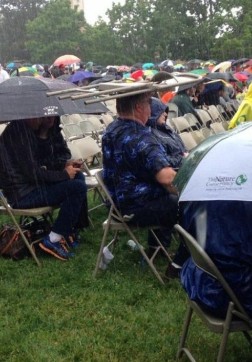 Lustige Menschen bei Regen - Stuhl als Regenschirm