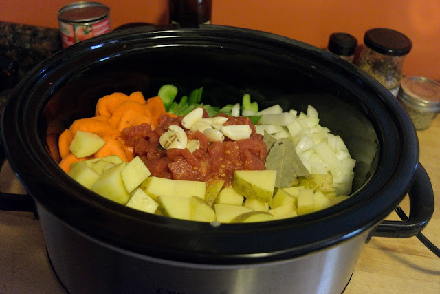 The vegetables, garlic, and bay leaf being added to the slow cooker. 