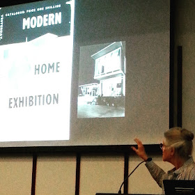 Mary Featherston giving a talk in front of a slide showing a flier of the Modern Home Exhibition.