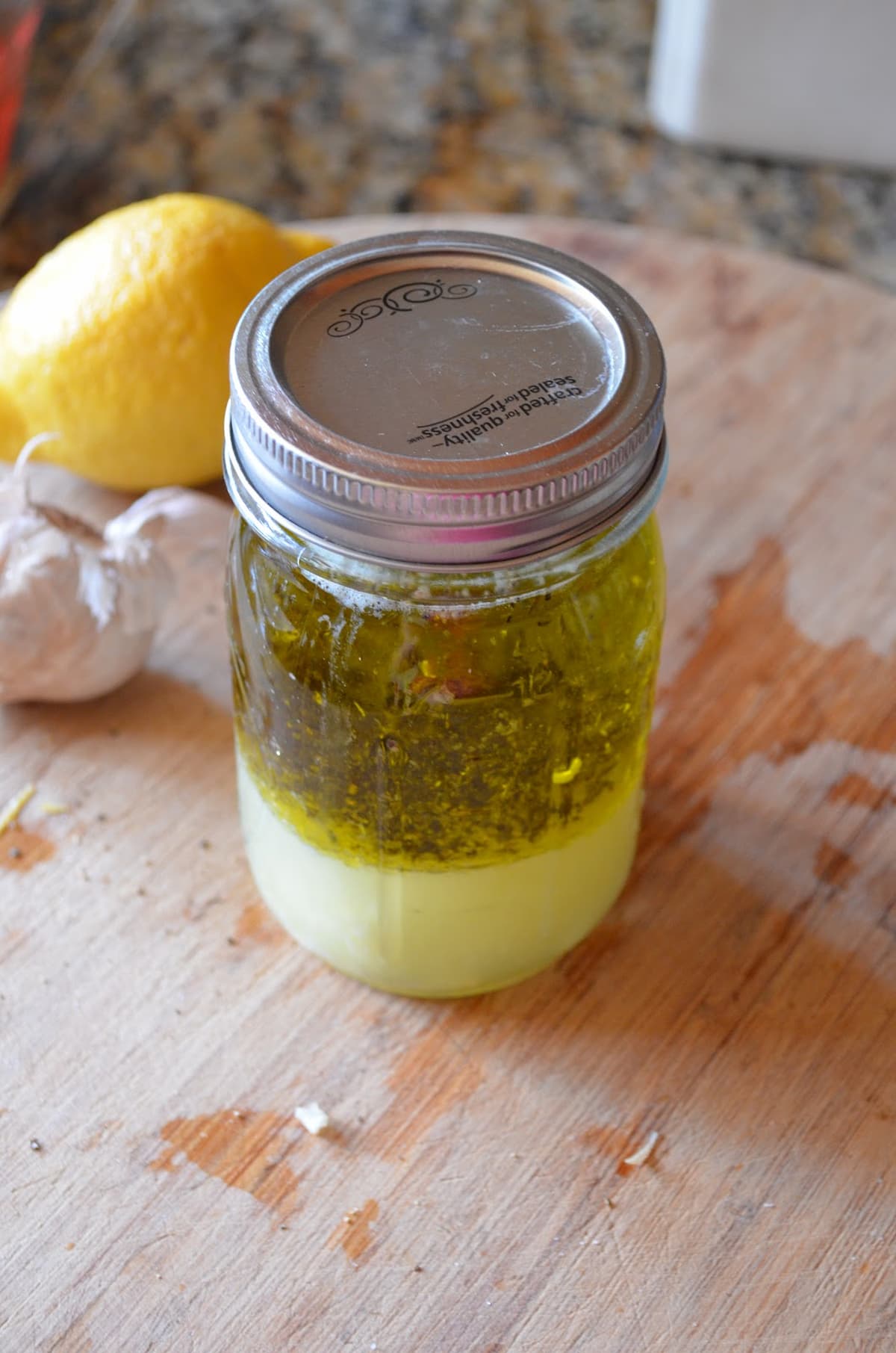 Lemon Vinaigrette recipe in a mason jar on a wooden cutting board.