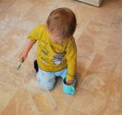 toddler sat on floor with cup, spoon and pearl barley