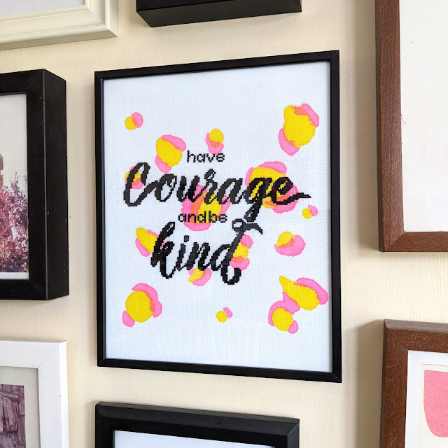 modern framed cross stitch with 'have courage and be kind' cross stiched in black on fabric with hand printed pink and yellow leopard print design in black frame