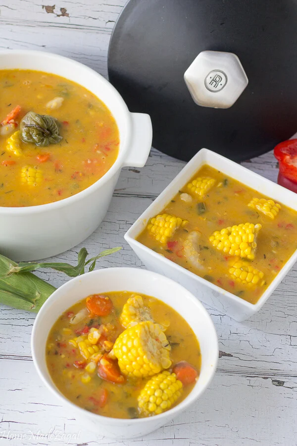 A bit white pot of Trinidad corn soup with a bowl serving