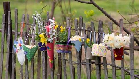 Different types of little flower-filled May Baskets hanging on a grey slatted fence.