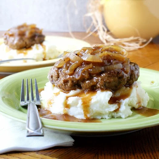 Side view of taditional mashed potatoes under salisbury steak on a green plate.