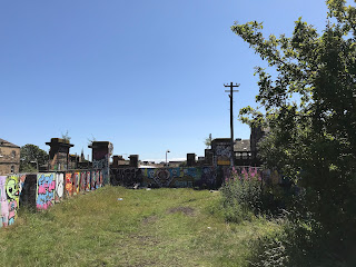 Site of the railway that led to the bridge - a grassy area leading down to a wall that blocks off the area where the bridge used to stand.  A lone telegraph pole stands in the corner by the wall.  Photo by Kevin Nosferatu for the Skulferatu Project