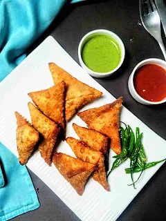 Serving onion samosa in s plate with fried green chili. Green chutney and sweet chutney in background