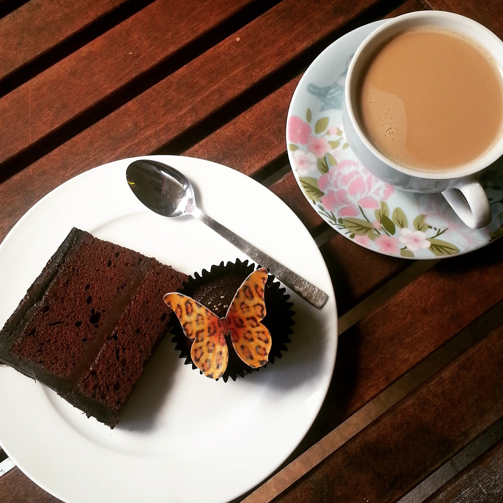 A slice of chocolate cakes, edible leopard print butterfly cupcake and a cup of nespresso coffee.