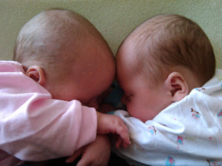 twin newborn baby girls sleeping with foreheads touching