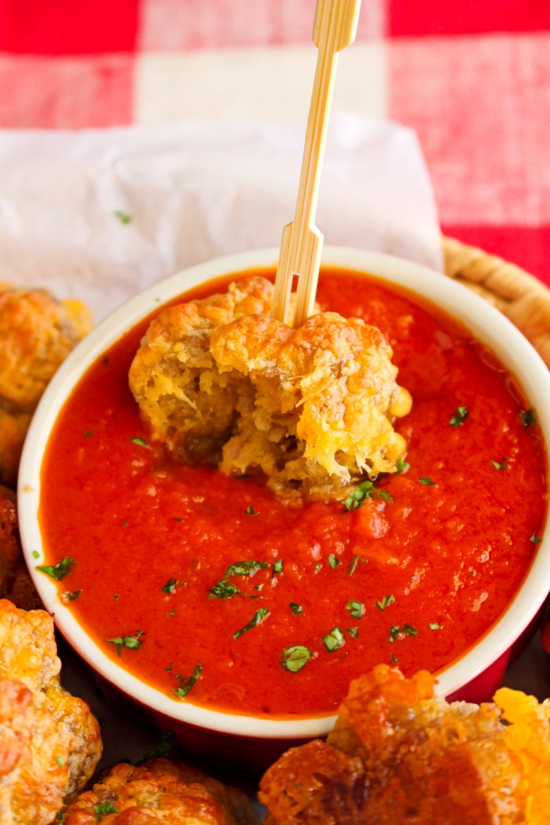 Side view of a sausage ball being dipped in marinara sauce.